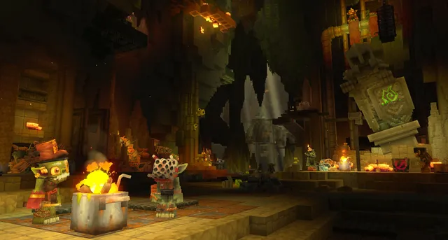 Goblins beside a fire in a vast cavern, with a glowing rune on a stone statue.